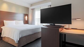 Una habitación de hotel con cama, escritorio y televisor de pantalla plana, y ventana con cortinas.