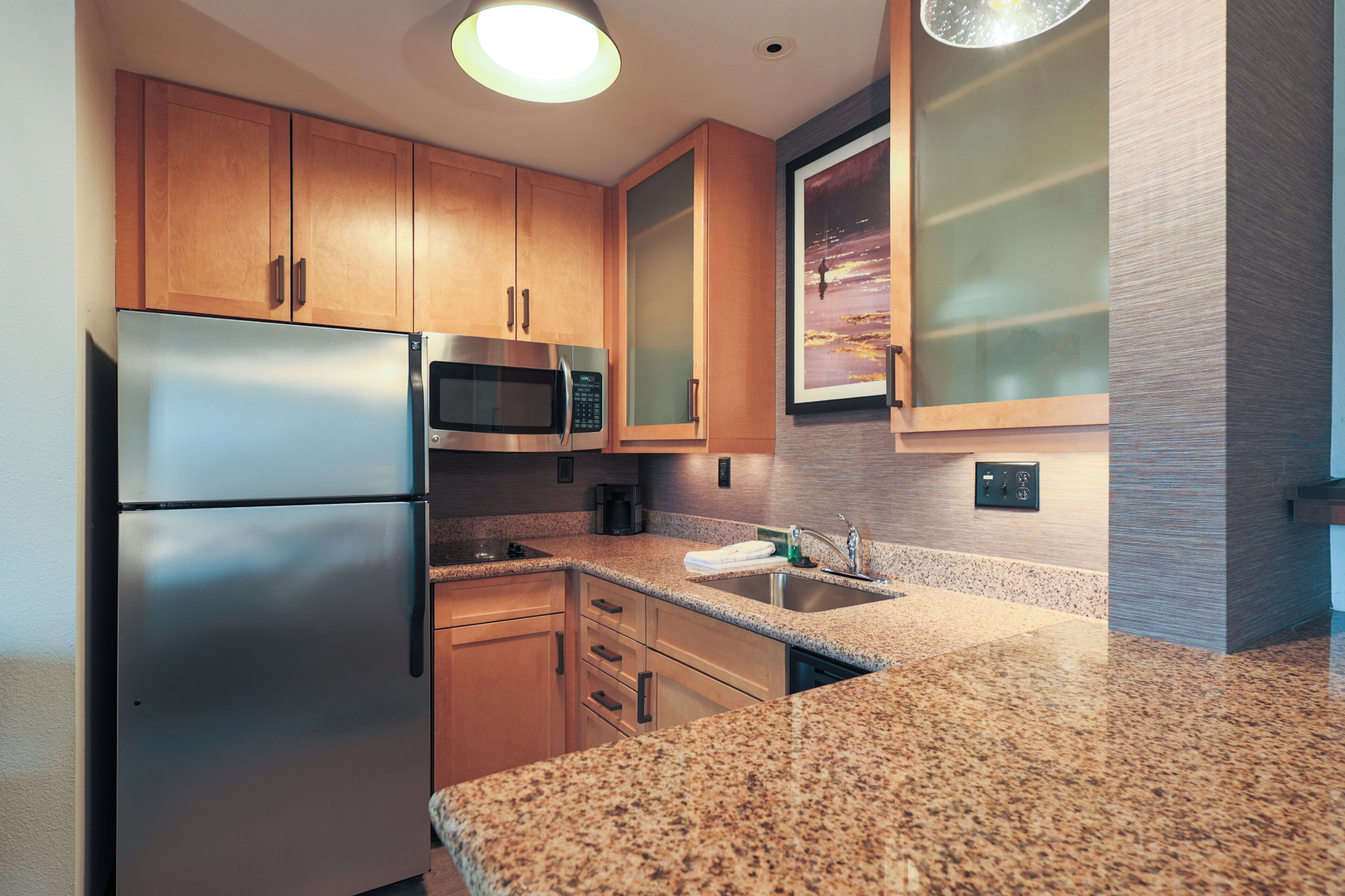A modern kitchen with stainless steel appliances, wooden cabinets, granite countertops, and a backsplash.
