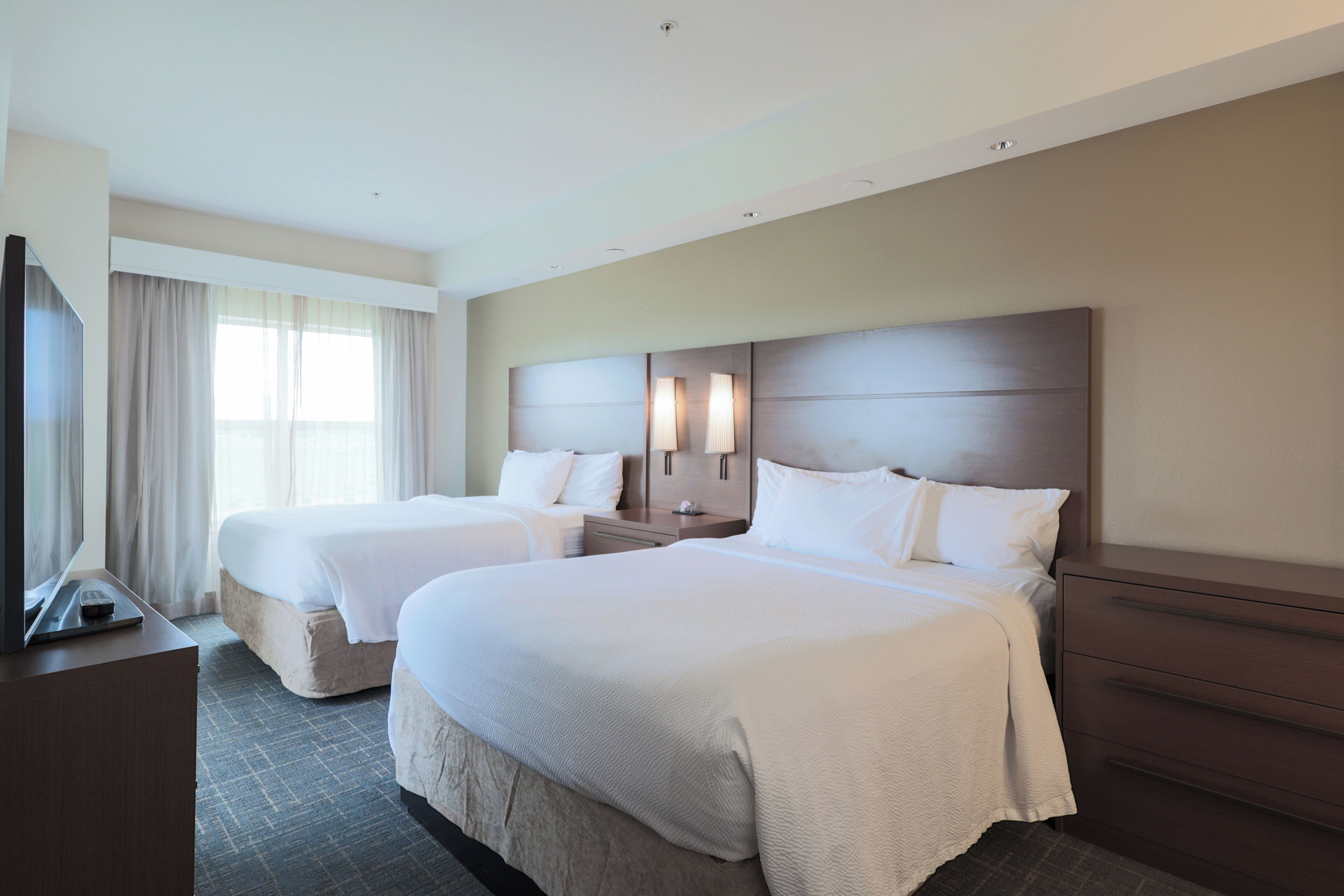 A hotel room with two beds, a TV, and a desk.