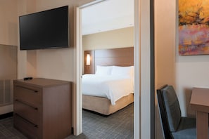 A hotel room with a bed, a desk, a television, and a painting on the wall.