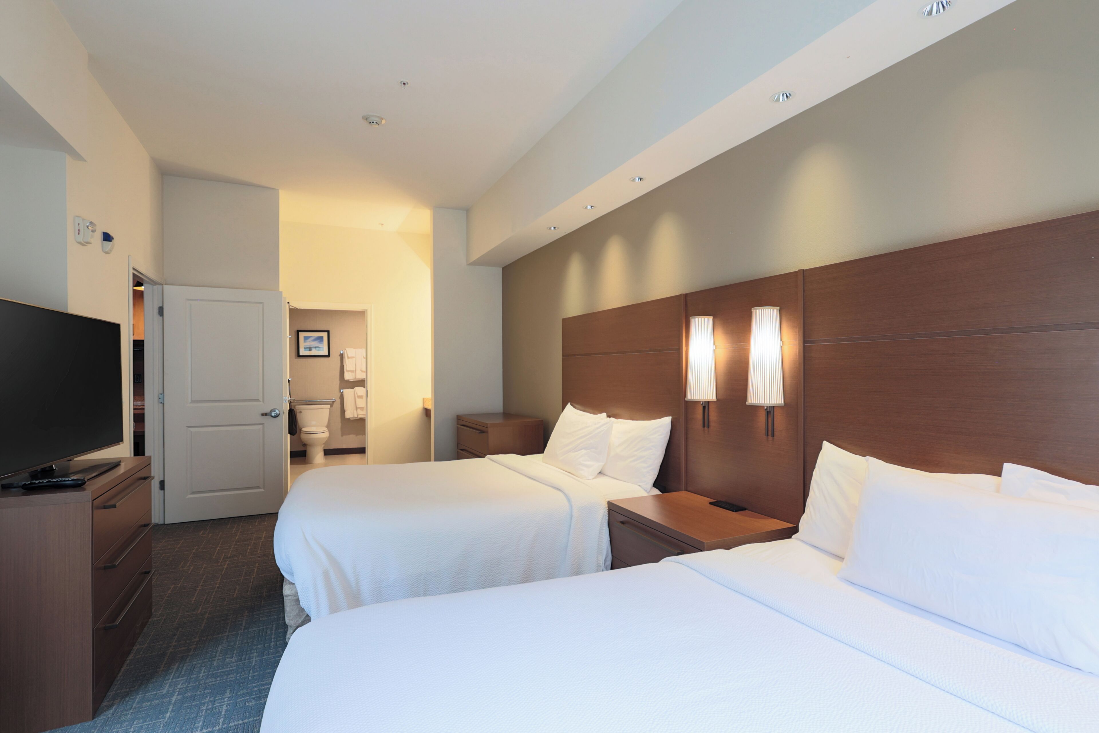 A hotel room with two beds, a television, and a bathroom visible through an open door.