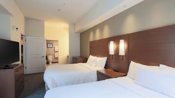 A hotel room with two beds, a television, and a bathroom visible through an open door.