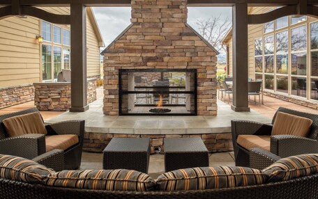 An outdoor patio with a stone fireplace, wicker furniture, and large windows.