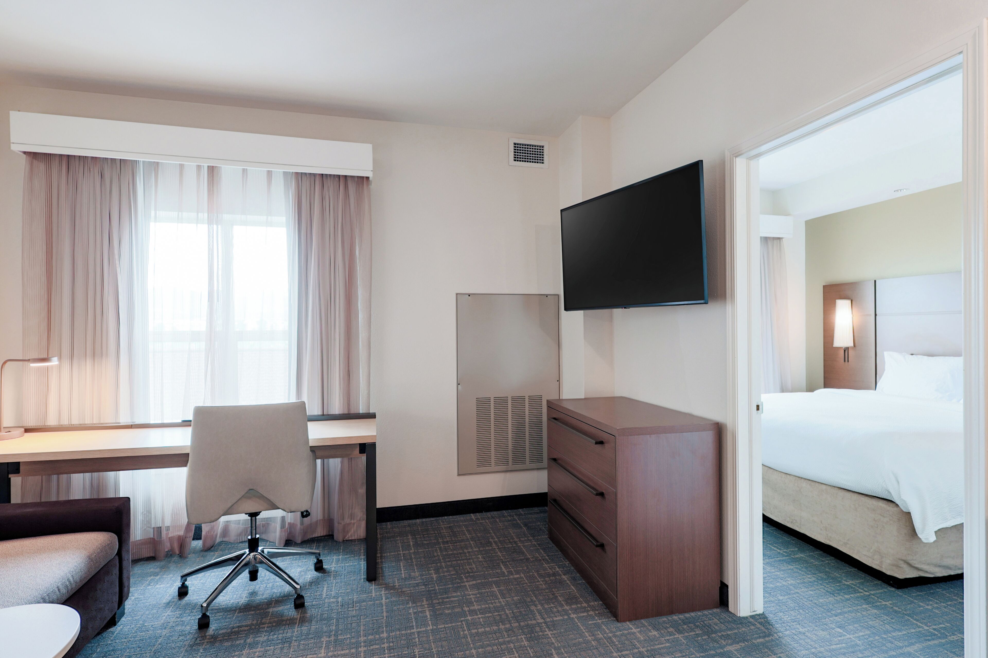 A hotel room with a bed, desk, chair, TV, and a window with curtains.