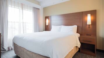 Quarto de hotel com uma cama grande, duas mesas de cabeceira e uma janela com cortinas.