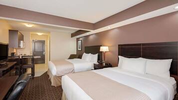 A hotel room with two beds, a desk, a chair, a TV, and a lamp.