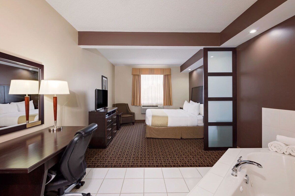 Une chambre d’hôtel comprenant un lit, un bureau avec une chaise, une télévision, une commode, une salle de bain avec une baignoire et un grand miroir.