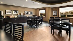 Un comedor amplio con varias mesas y sillas, una zona de cocina con dispensadores de alimentos y cuadros en las paredes.