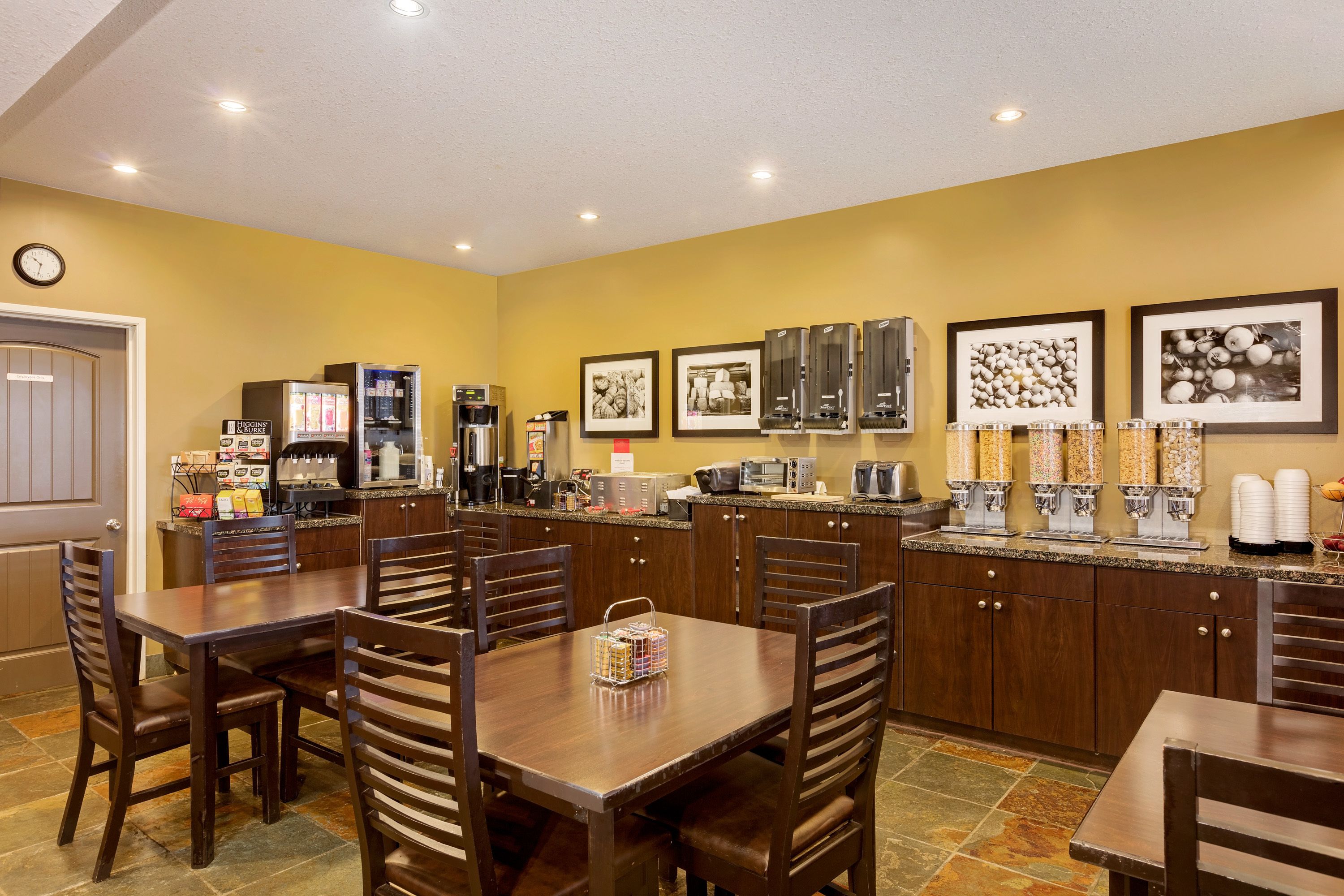Un comedor de hotel con mesas y sillas de madera, una máquina de café y un microondas.