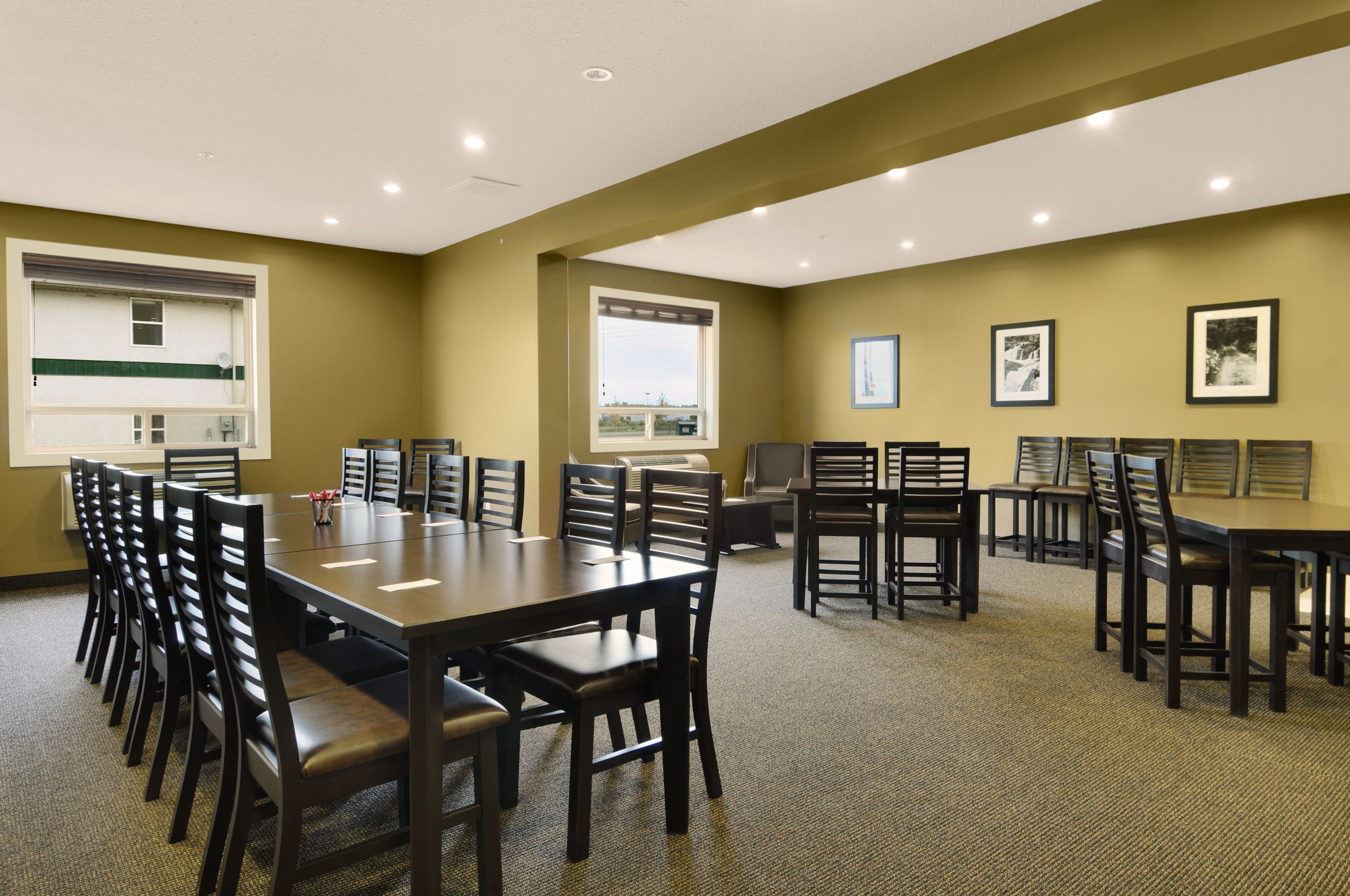 A conference room with multiple tables and chairs, large windows, and framed pictures on the walls.
