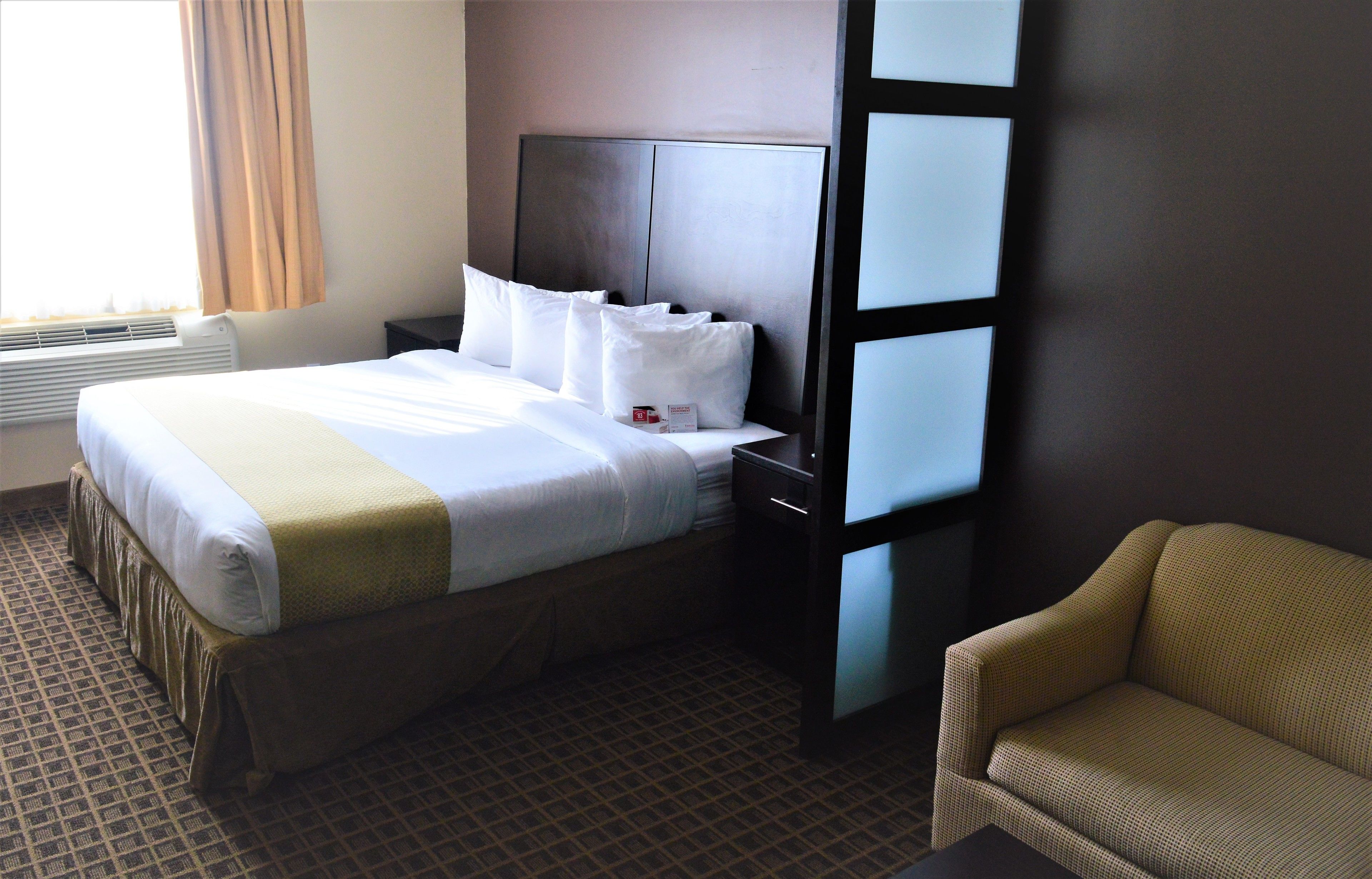 A hotel room with a large bed, a nightstand, a chair, and a window with curtains.