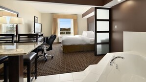 Habitación de hotel con cama, escritorio con silla, televisor, ventana grande con cortinas y bañera.