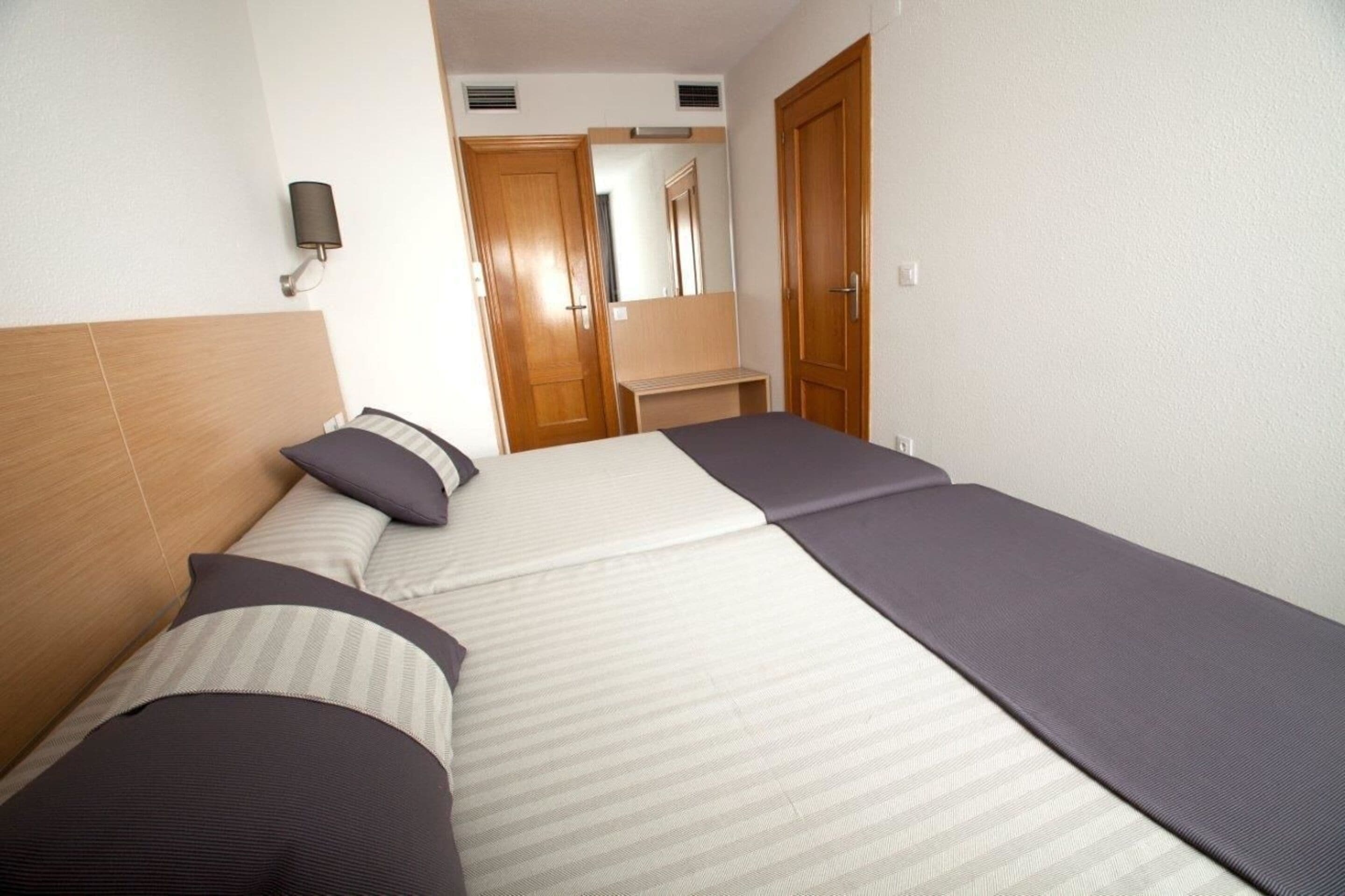 Ein Hotelzimmer mit Bett, Nachttisch, Spiegel und Tür.