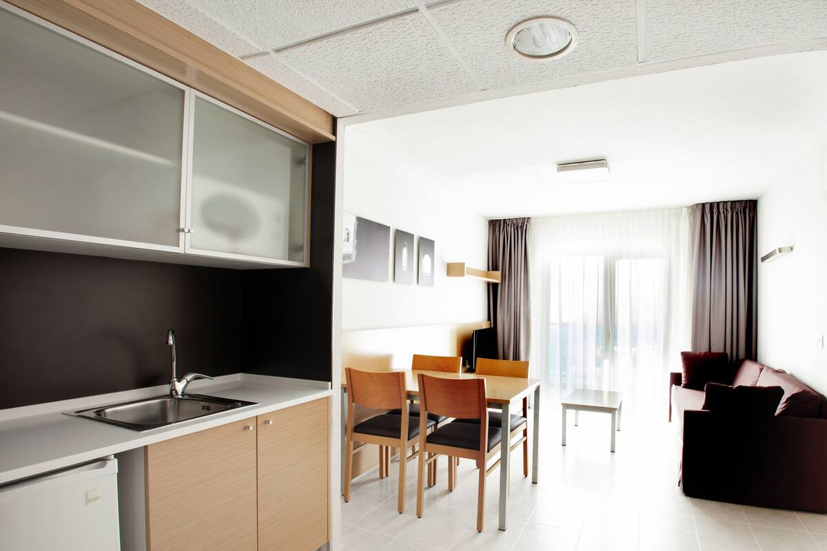 A modern kitchen with a sink, cabinets, and a dining area with chairs and a table.