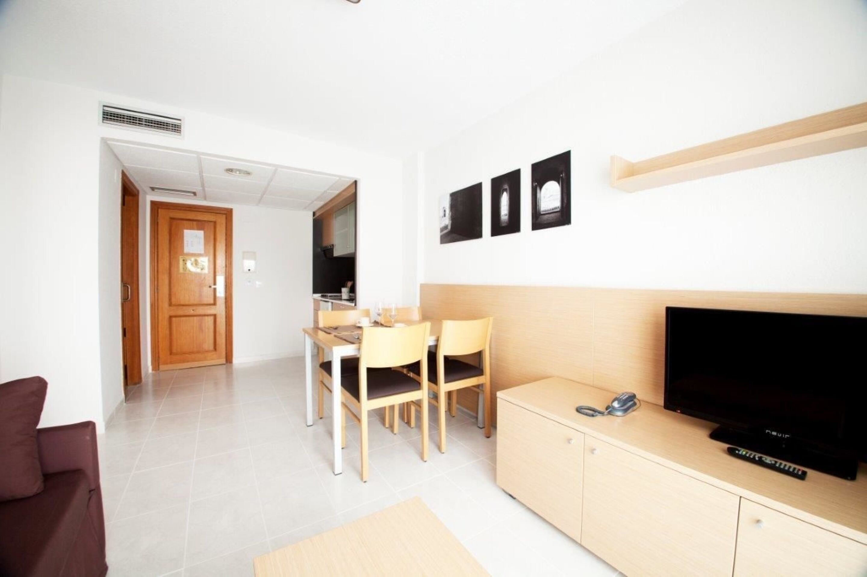 Una sala de estar moderna con televisor de pantalla plana, muebles de madera y un comedor con sillas y una mesa.