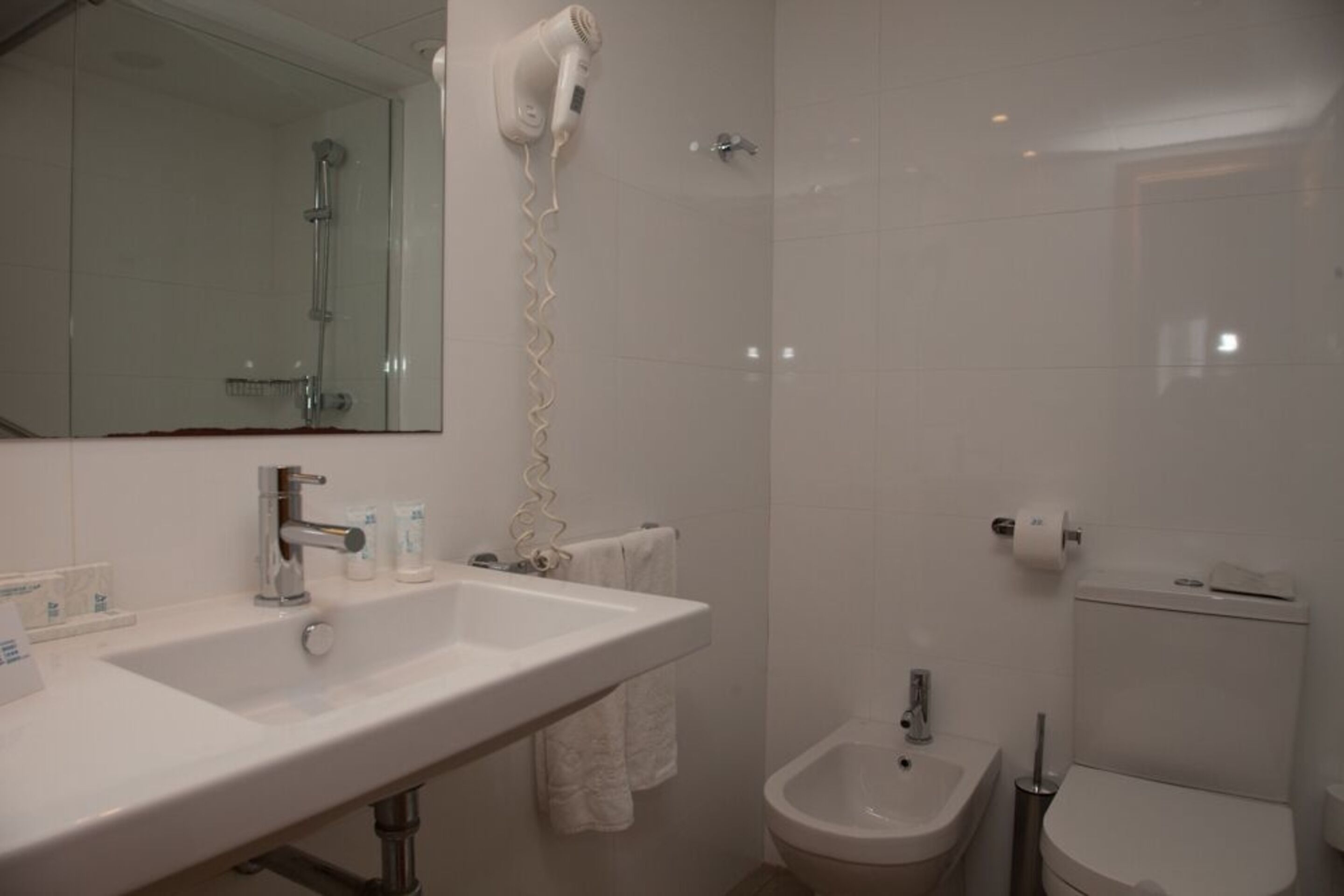 Un baño con lavamanos doble, secador de pelo, bidé y retrete.