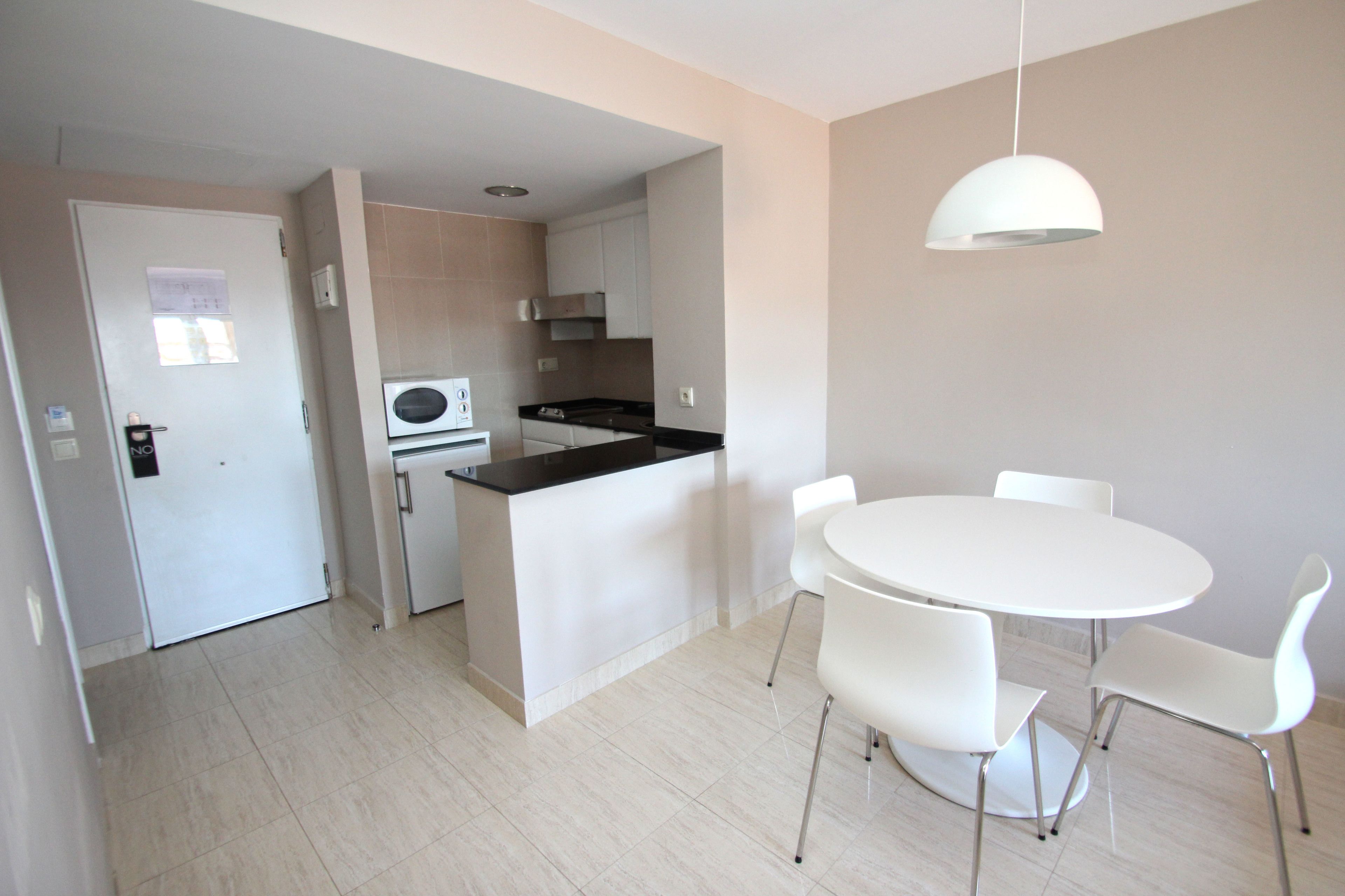 Una cocina moderna con una isla central, sillas blancas alrededor de una mesa redonda y una lámpara colgante.