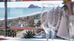 Vista desde un balcón sobre una playa con una isla rocosa en la distancia.