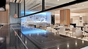 Un restaurante moderno con una barra alargada, sillas blancas y un amplio ventanal con vistas a la ciudad.