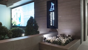 Entrada de un hotel con un gran cartel digital, un letrero de neón del hotel y un macizo de flores.