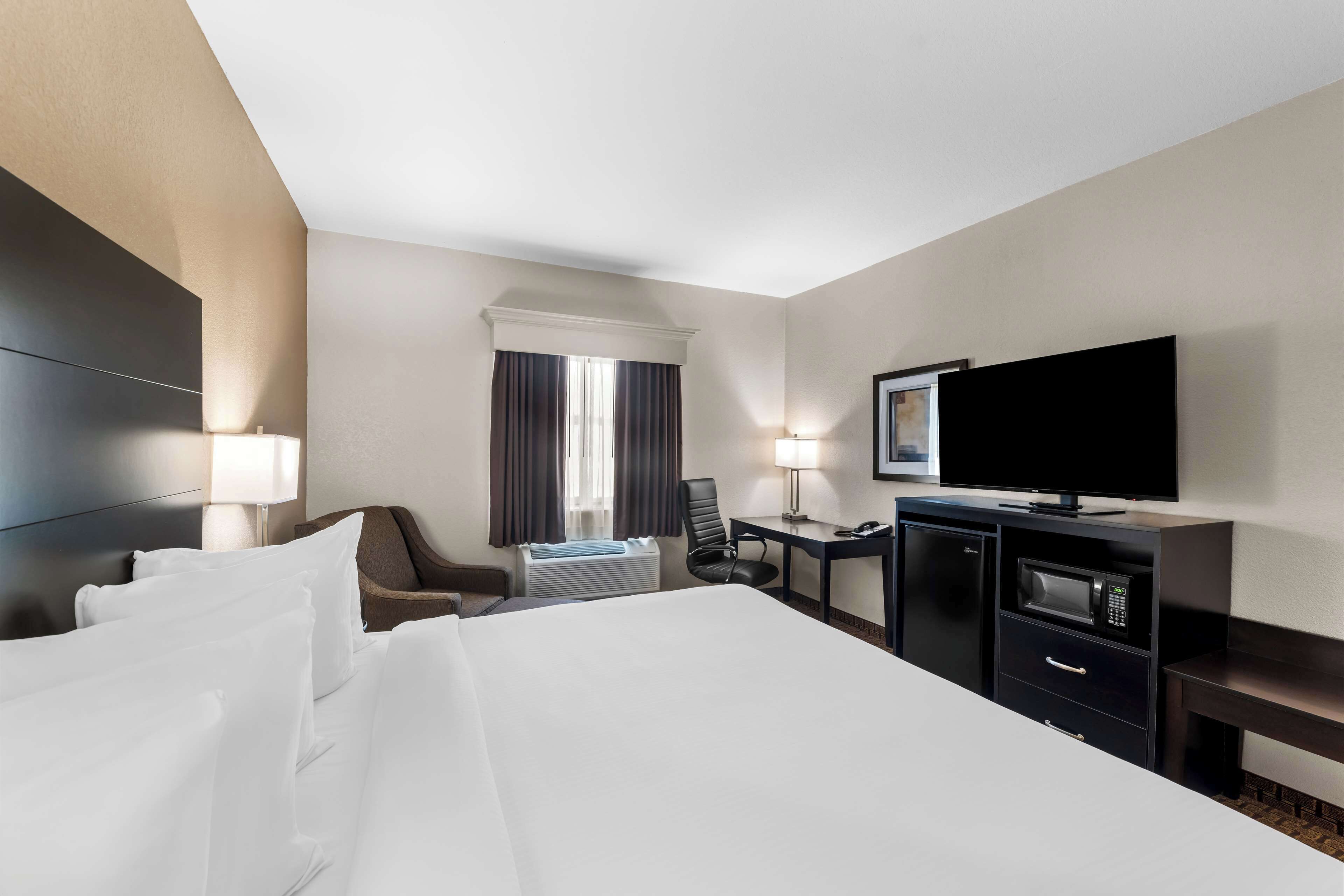 A hotel room with a bed, a desk with a flat-screen TV, a microwave, and a chair.
