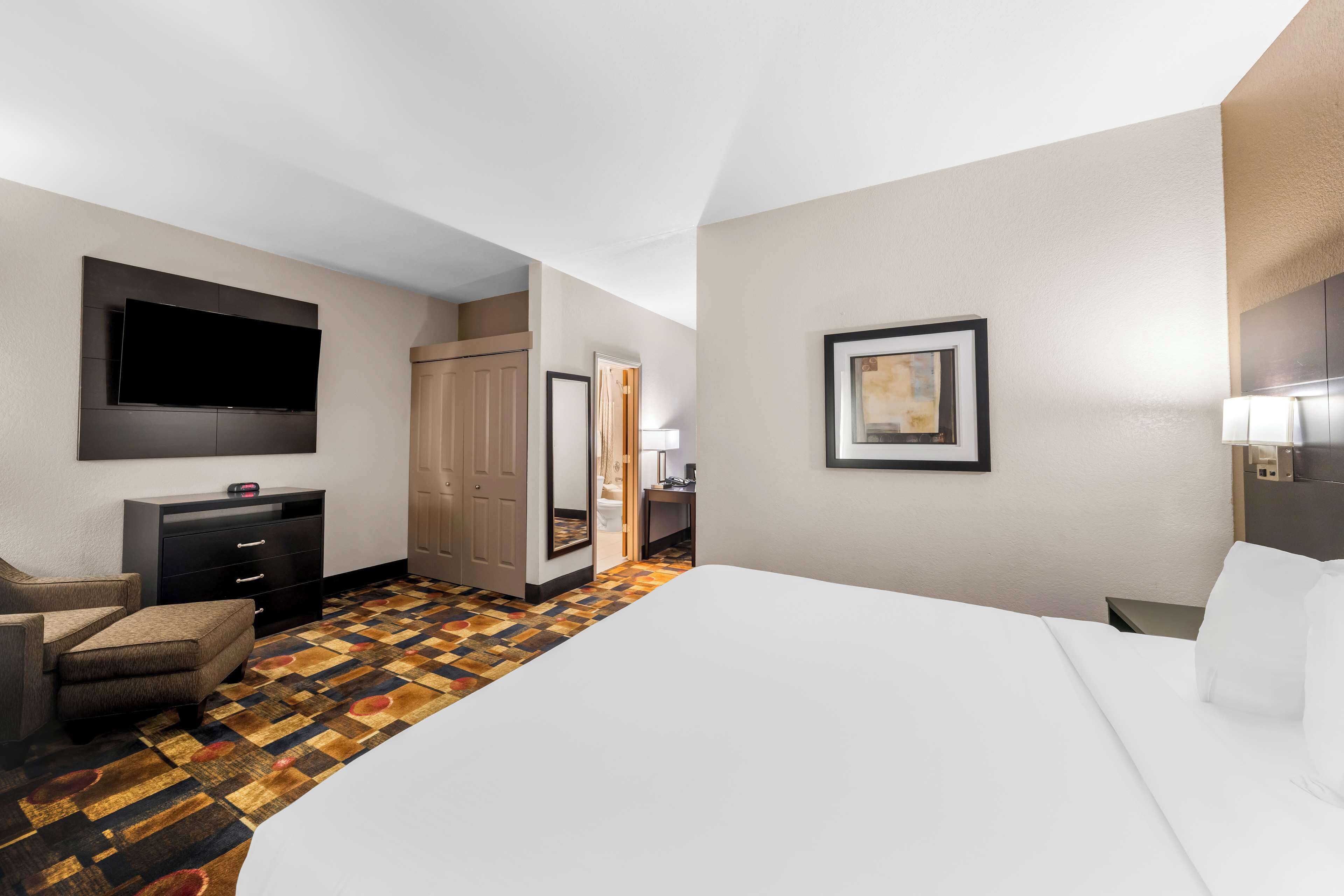 Habitación de hotel con una cama grande, un televisor de pantalla plana en la pared, un escritorio con una silla y un armario.