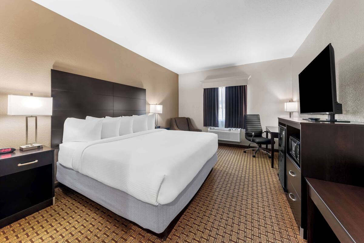 A hotel room with a large bed, a desk with a flat-screen TV, a chair, and a desk lamp.