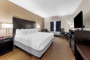 A hotel room with a large bed, a desk with a flat-screen TV, a chair, and a desk lamp.