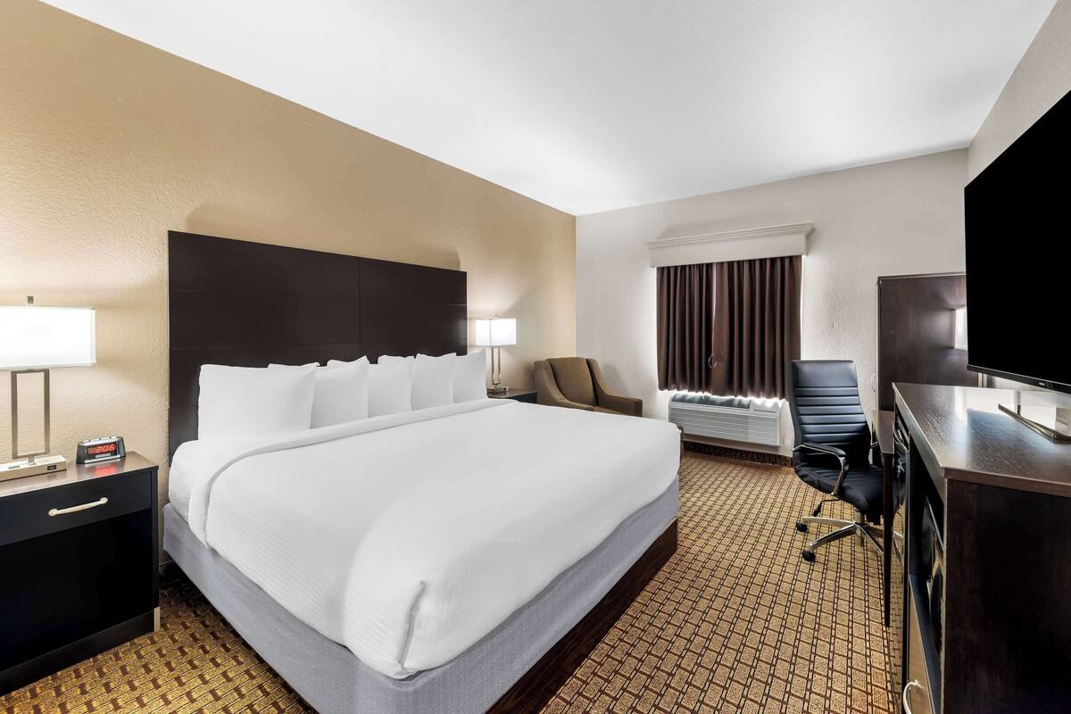 A hotel room with a large bed, a desk with a flat-screen TV, a chair, and a window with curtains.