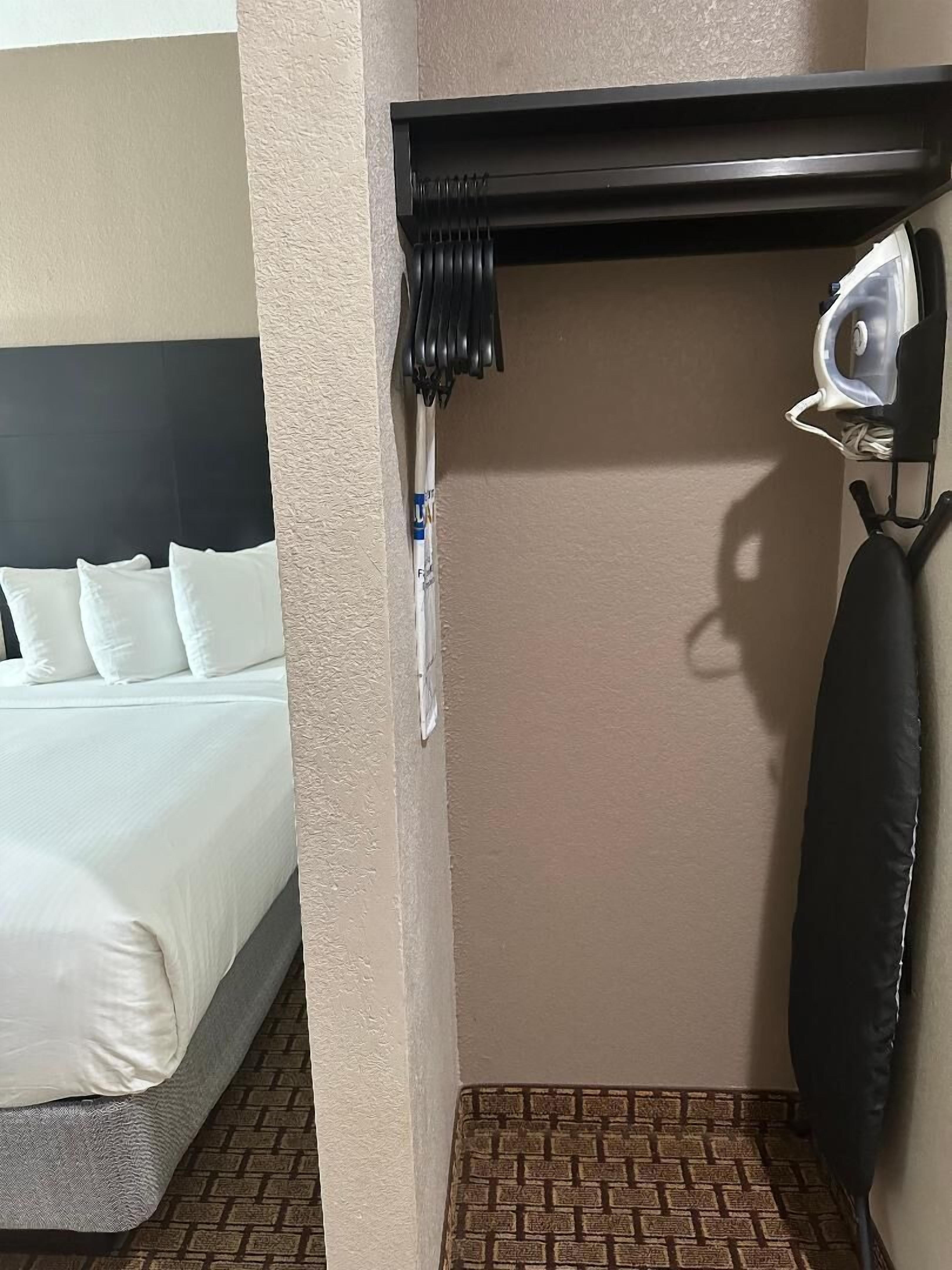 A hotel room with a bed, a wall-mounted ironing board, and a hanging garment.