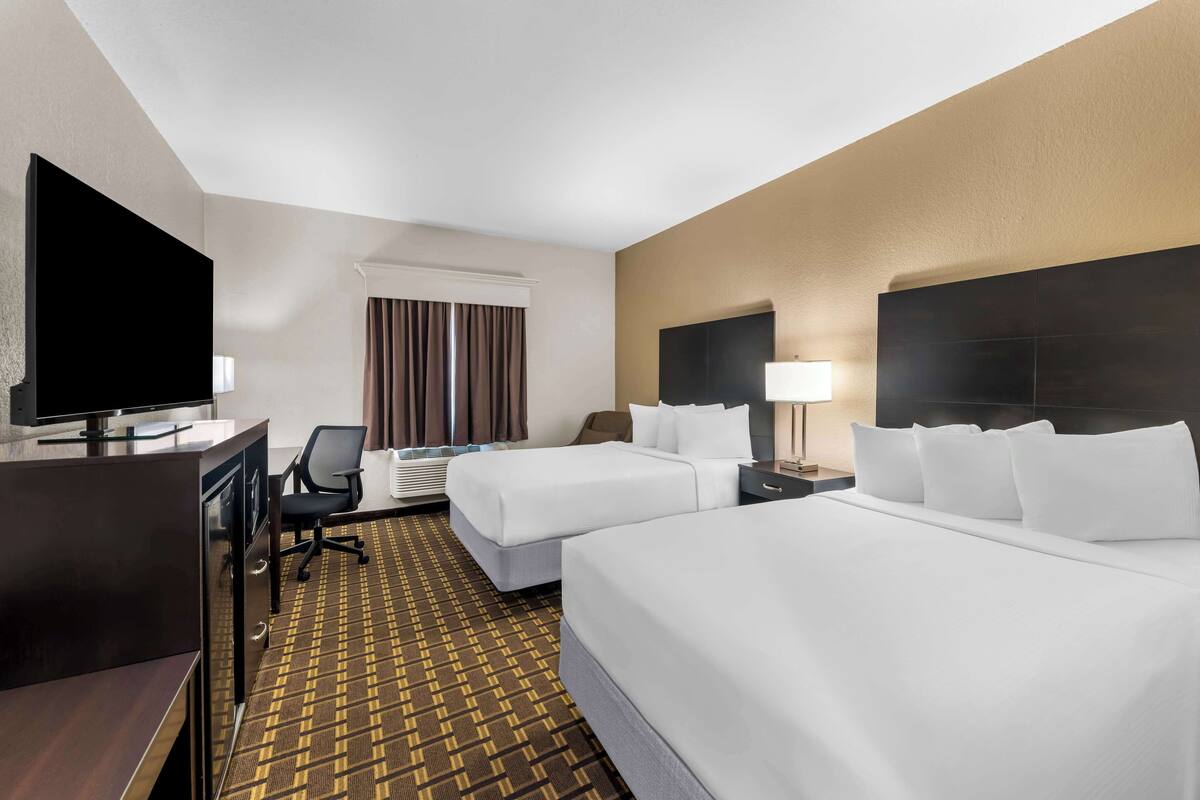 A hotel room with two beds, a desk, a TV, and a window with curtains.