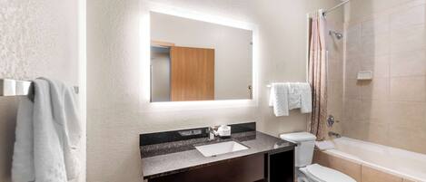 A modern bathroom with a dark vanity, a white sink, a toilet, and a bathtub.