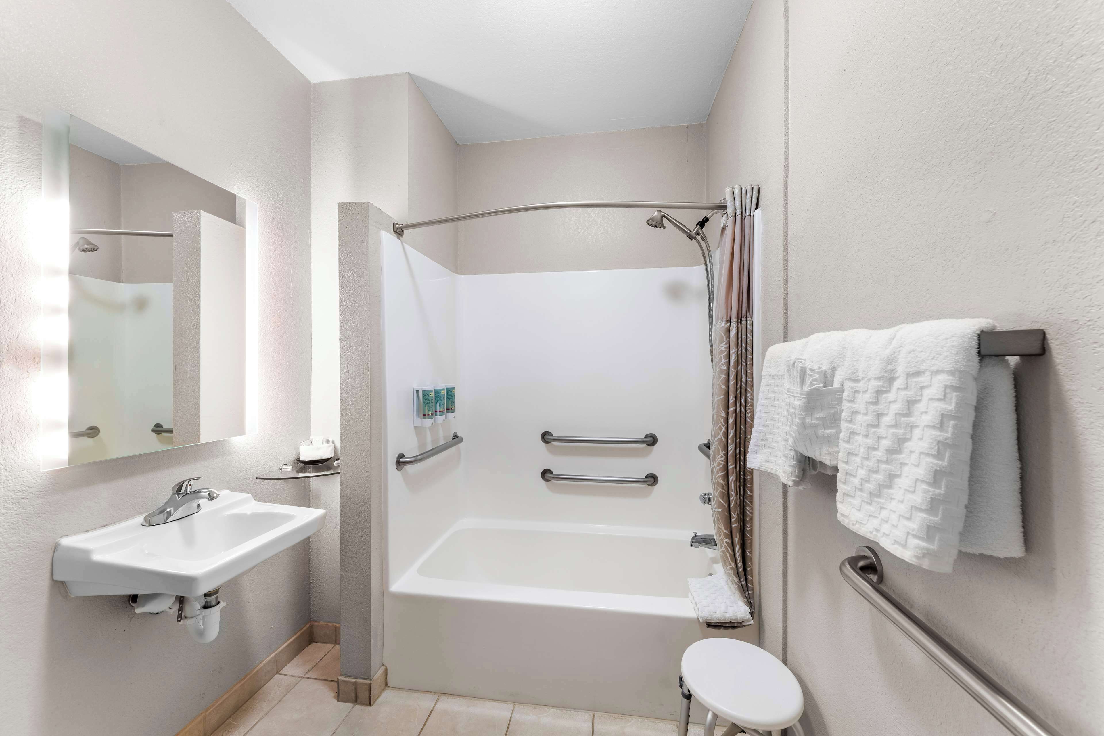 Un baño moderno con lavabo, bañera y ducha. Incluye barras de apoyo y un perchero para toallas.