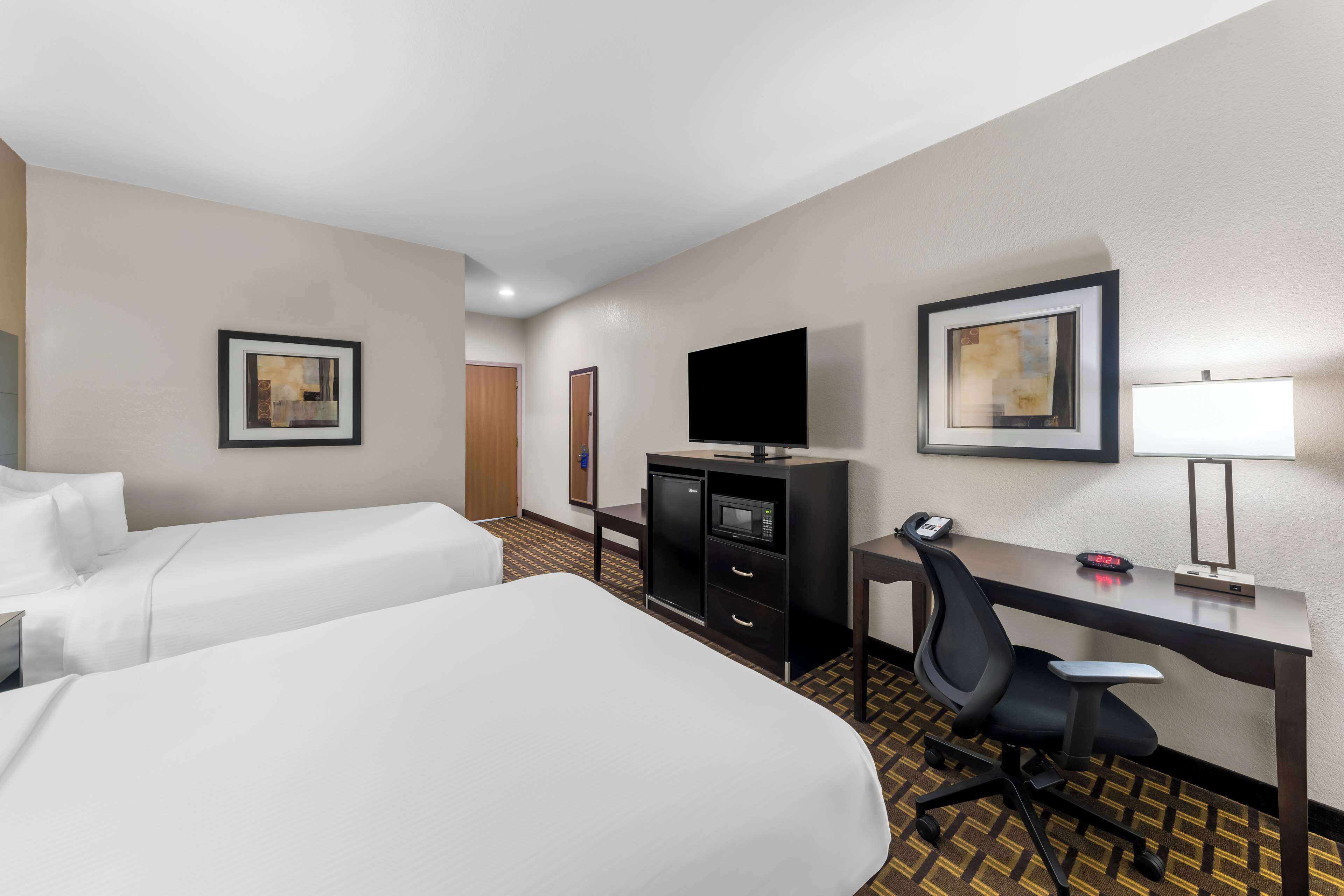 A hotel room with two beds, a desk, a chair, a TV, a desk lamp, and a microwave.