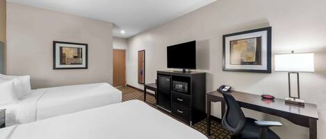 A hotel room with two beds, a desk, a chair, a TV, a desk lamp, and a microwave.