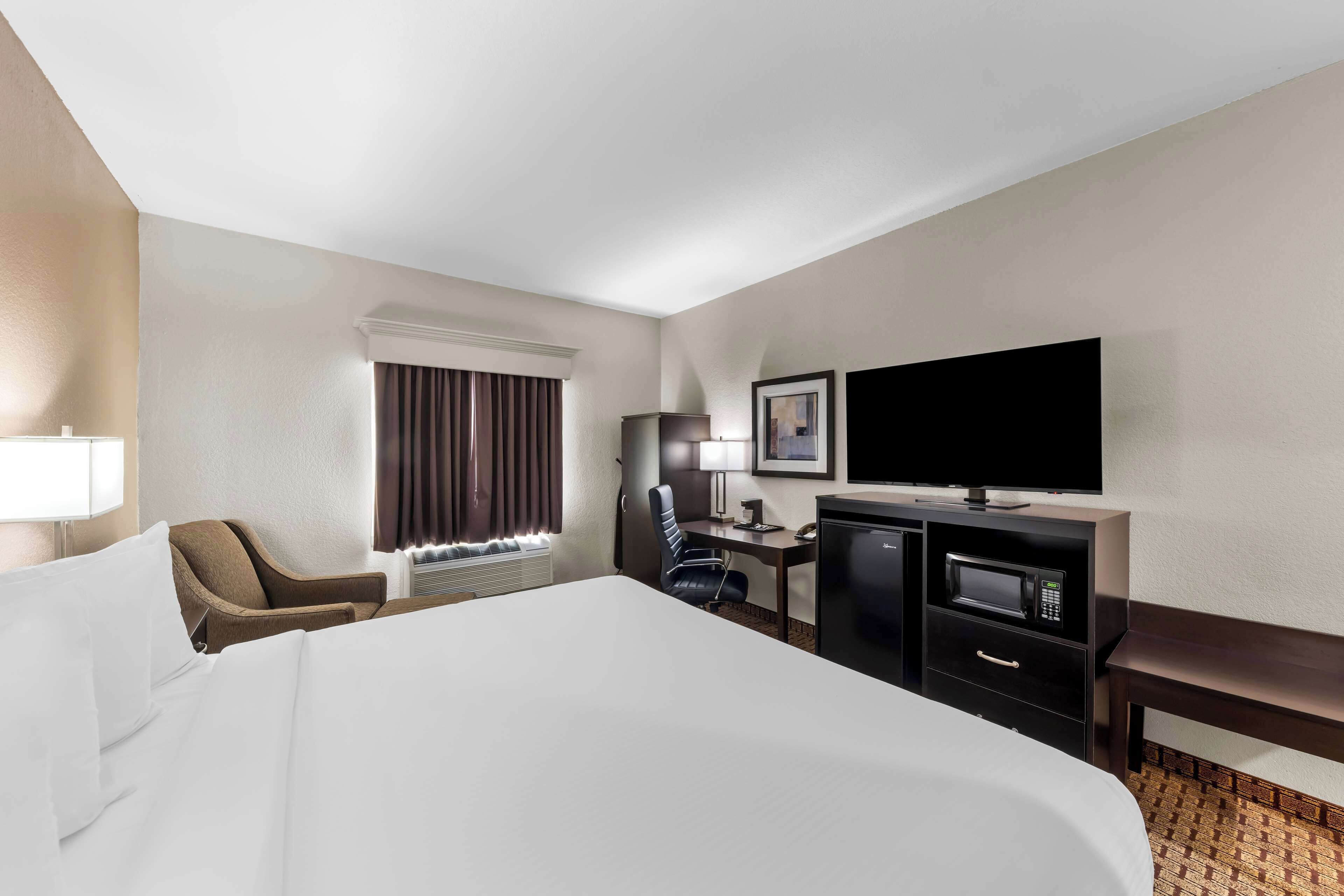 A hotel room with a large bed, a desk with a computer, a flat-screen TV, a microwave, and a chair.