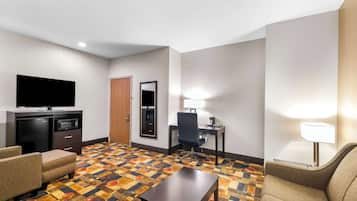 A hotel room with a flat-screen TV, a desk with a chair, a microwave, a small refrigerator, and a patterned carpet.
