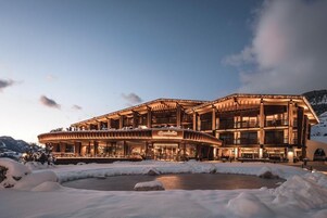 Un hotel grande de varios pisos con fachada curva, zona de estar al aire libre y paisaje cubierto de nieve.