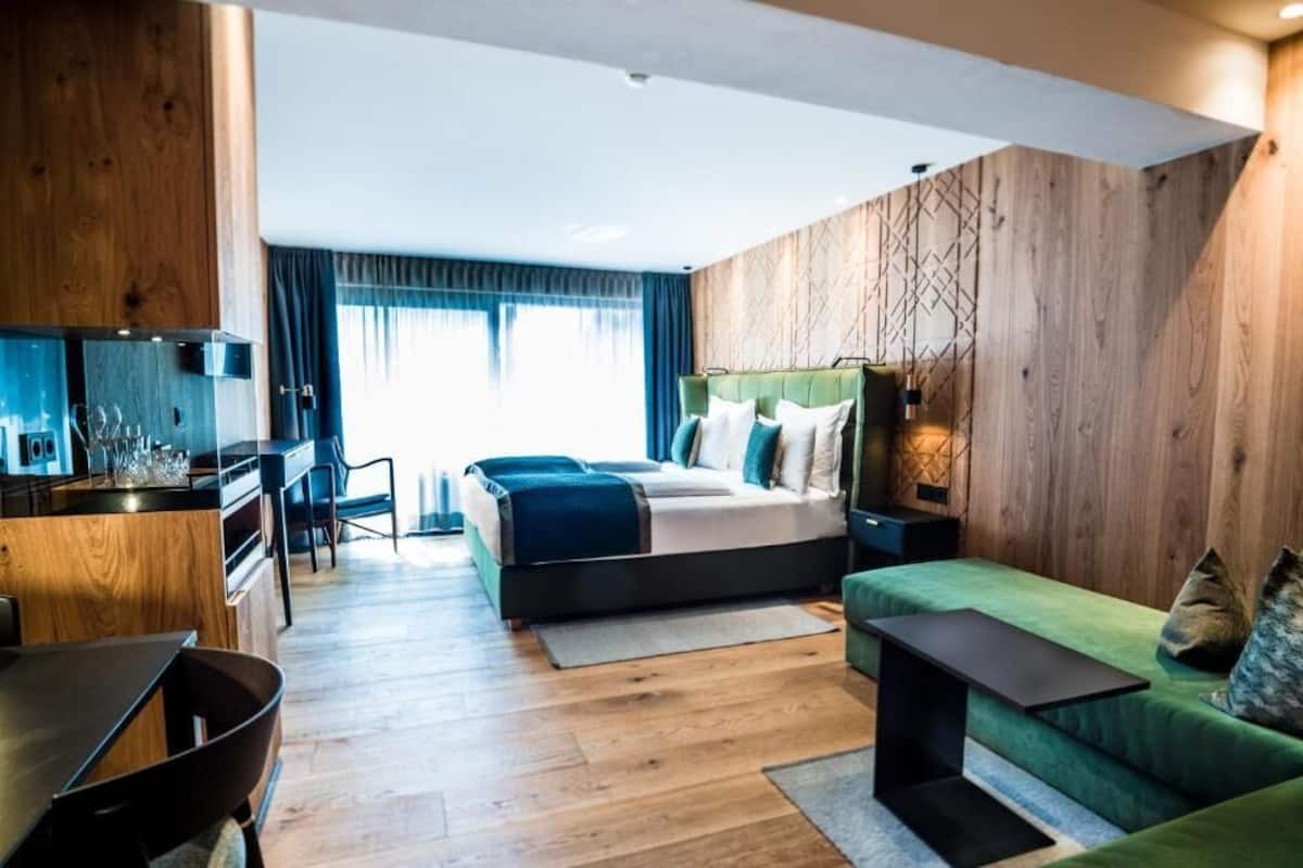 Une chambre d’hôtel moderne avec un mur d’accent en bois, un lit avec une tête de lit verte, un canapé vert et un petit espace bureau.