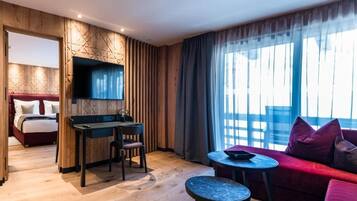Ein Hotelzimmer mit einem Bett, einem Schreibtisch mit Stuhl, einem kleinen Tisch, einer Couch und einem großen Fenster mit Vorhängen.