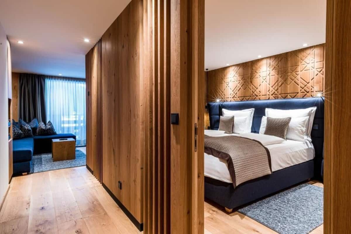 Une chambre moderne avec une armoire en bois, un lit doté d’une tête de lit à motifs, un canapé bleu et une petite table d’appoint en bois.