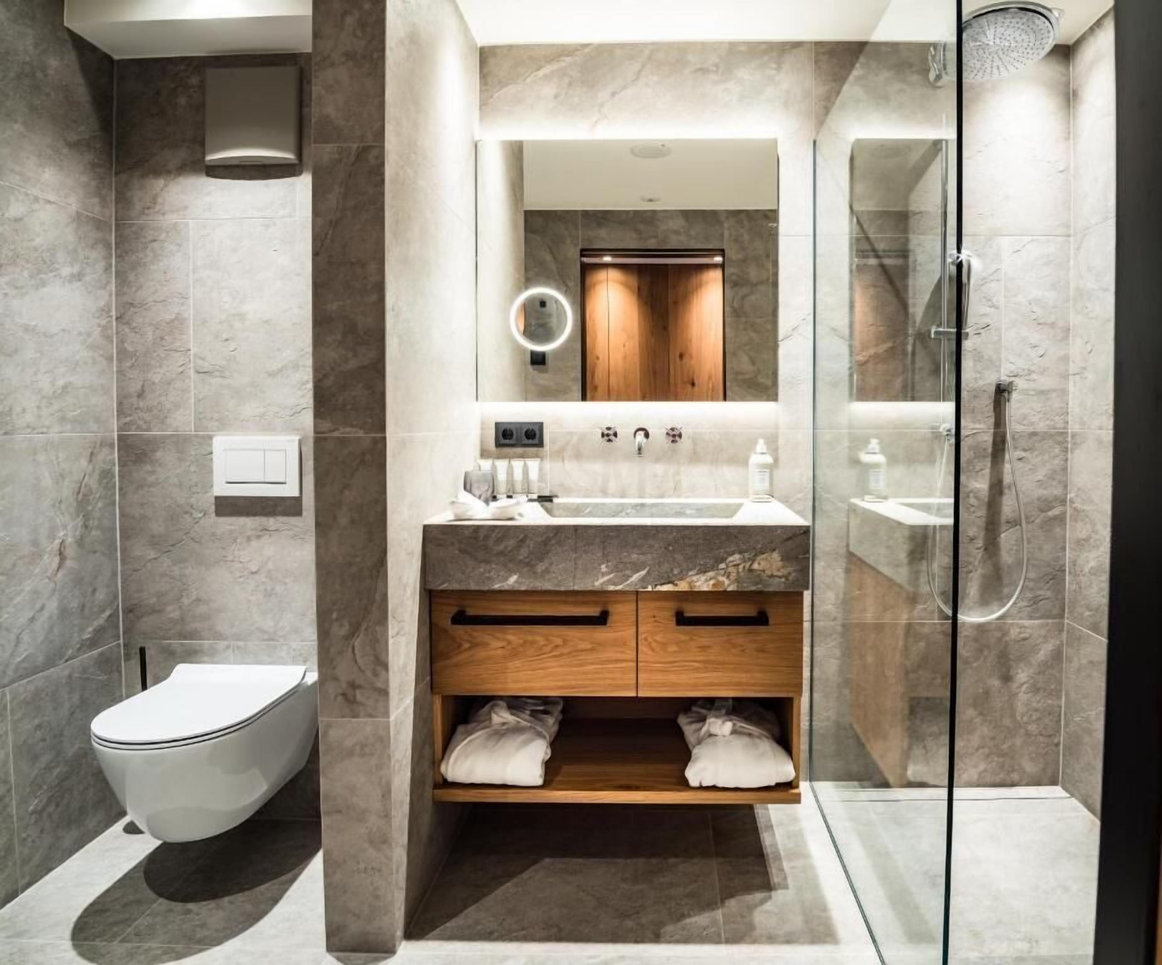 Un baño moderno con lavamanos de mármol, tocador de madera y cabina de ducha con mampara de vidrio.