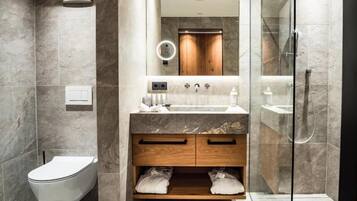 Un baño moderno con lavamanos de mármol, tocador de madera y cabina de ducha con mampara de vidrio.
