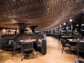 Un interior de restaurante moderno con techo de madera, mesas redondas y asientos cómodos.