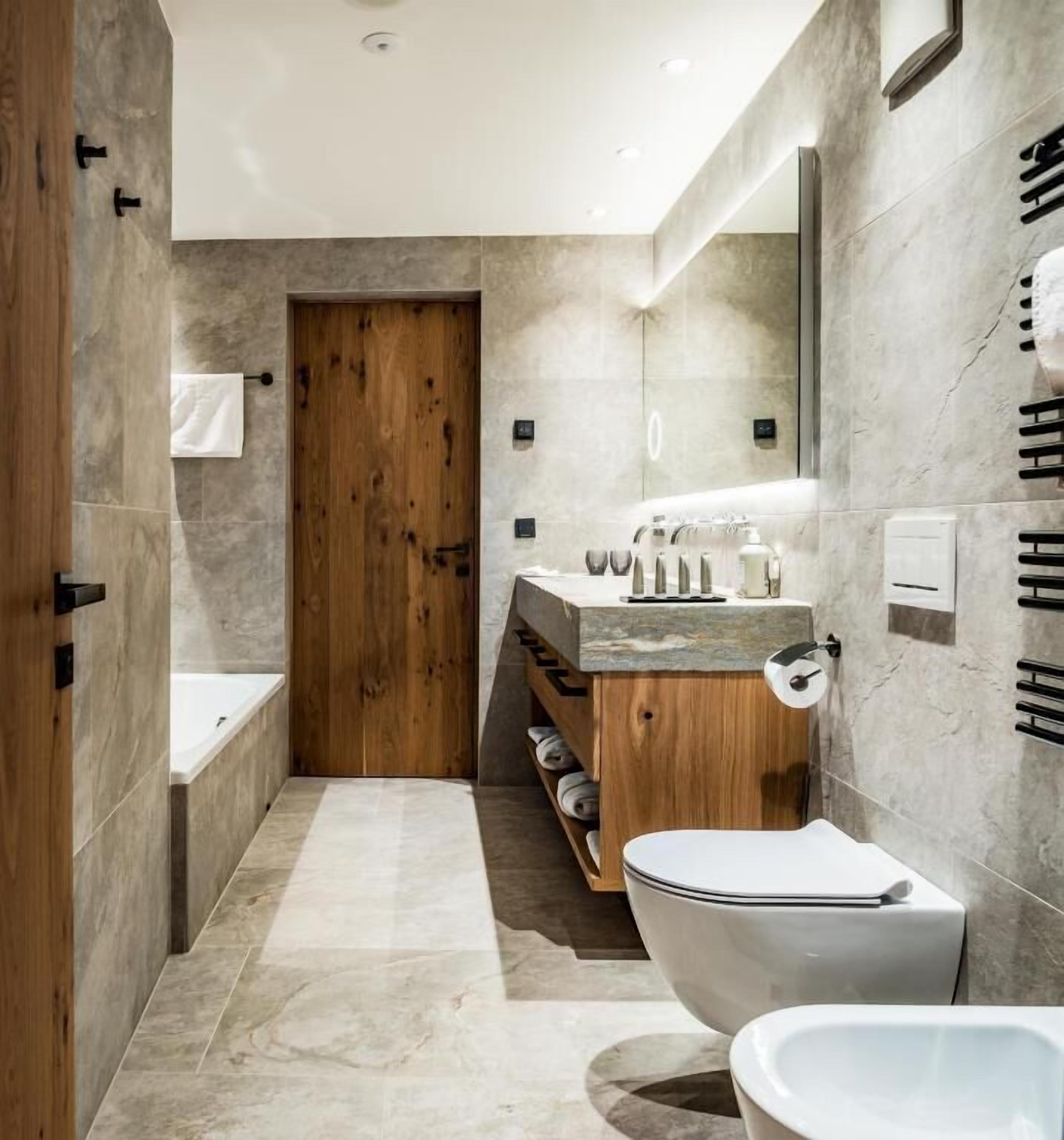 Ein modernes Badezimmer mit Holztür, freistehender Badewanne, Toilette und Waschtisch mit Spiegel.