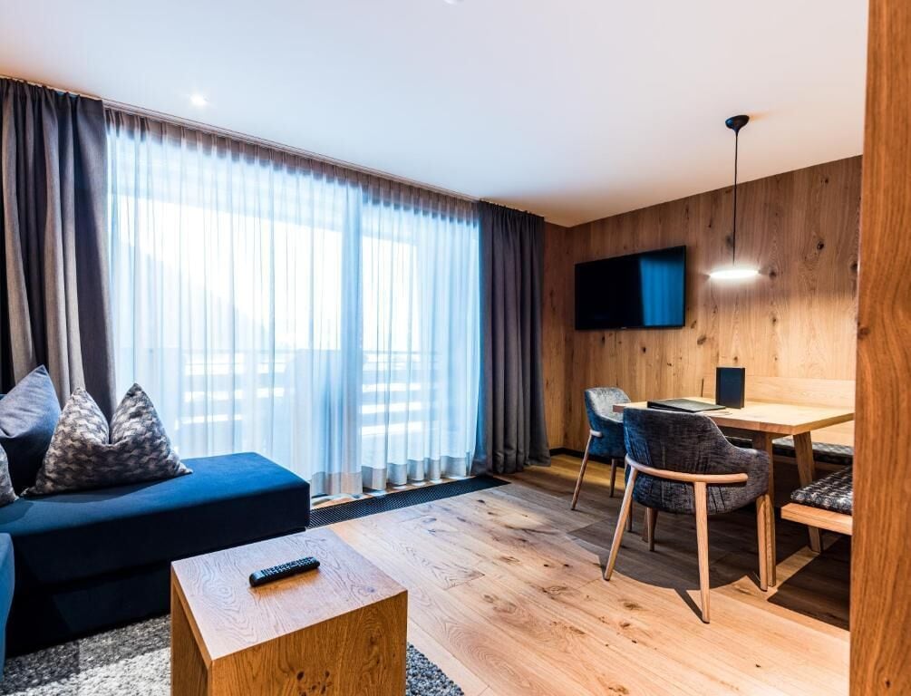 A modern living room with a sofa, a coffee table, a dining area with a table and chairs, and a TV mounted on the wall.