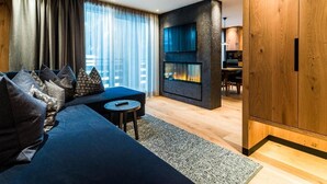 A modern living room with a dark blue sofa, a small round table, and a fireplace. - Hotel Granbaita Dolomites (Selva di Val Gardena)
