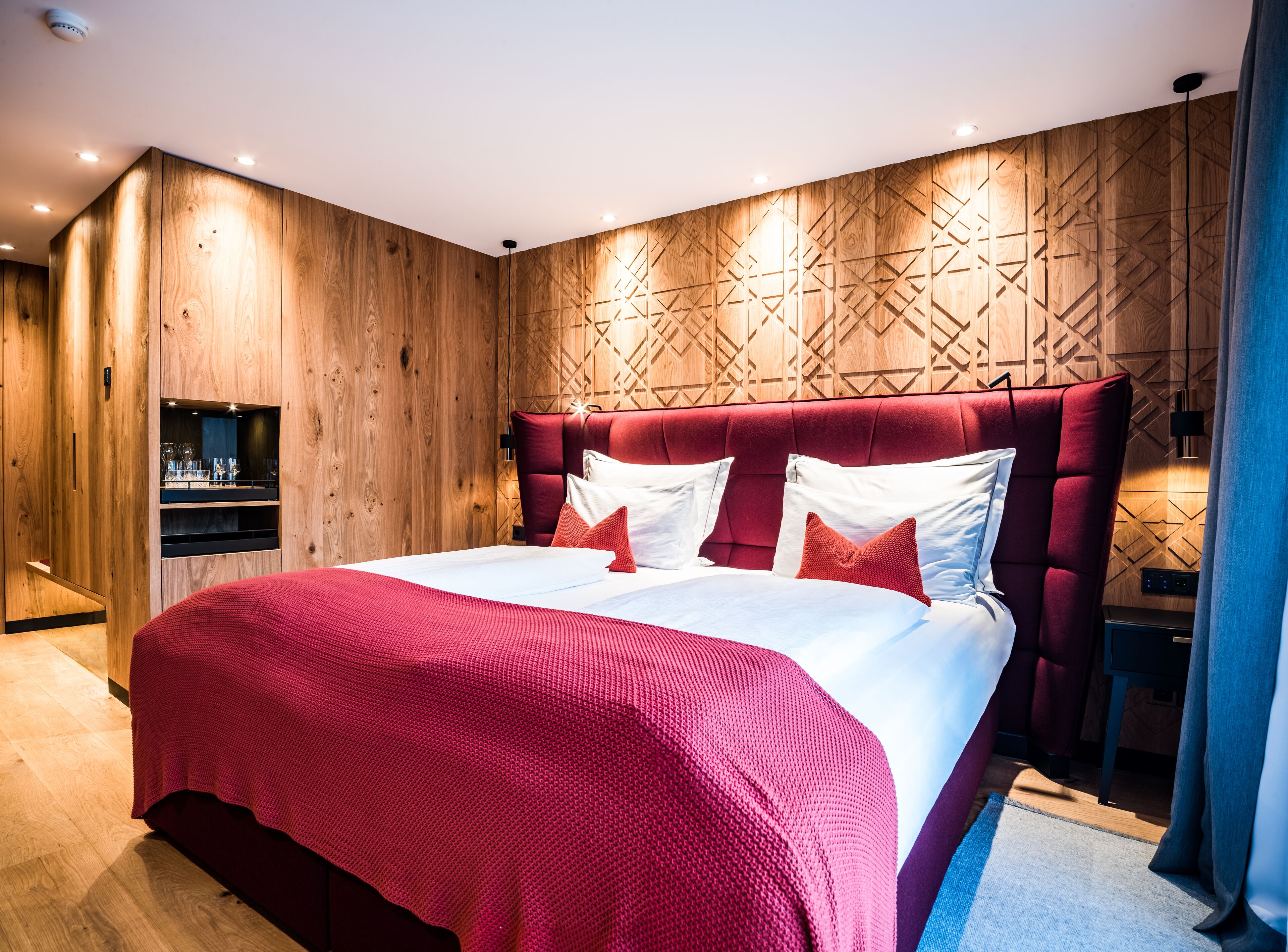 A modern bedroom with a large bed, wooden panel walls, and built-in shelves.