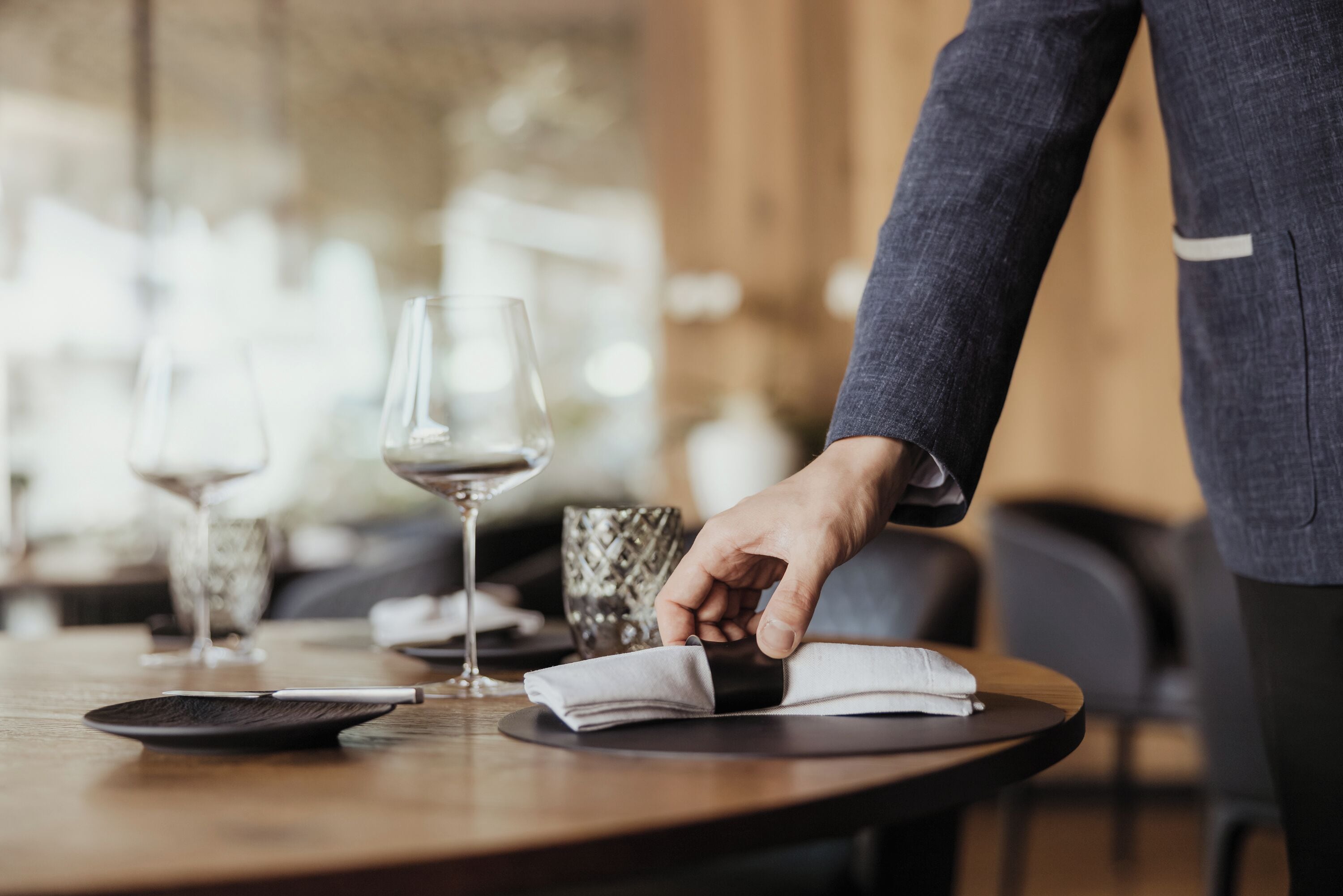 Una persona colocando una servilleta sobre una mesa redonda con una copa de vino y un cuenco decorativo.