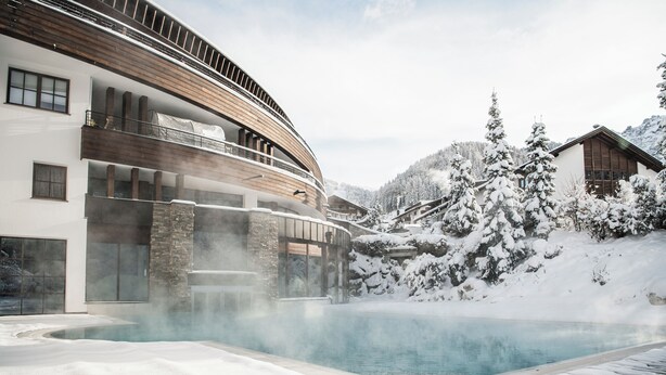 A modern building with a pool surrounded by snow-covered landscape. - Hotel Granbaita Dolomites (Selva di Val Gardena)